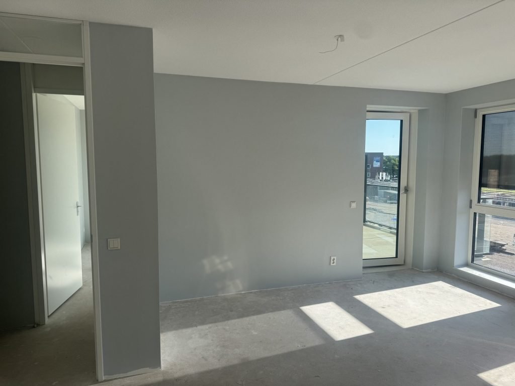 Lege kamer in een nieuwbouwhuis met kale wanden en een betonvloer, klaar voor het behangwerk