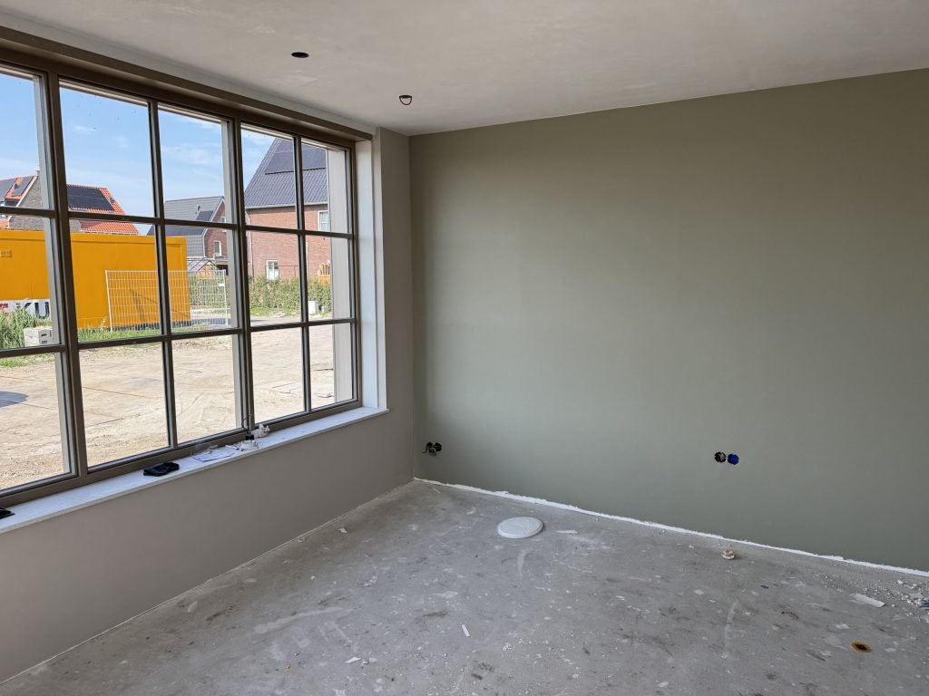 Nieuwbouwkamer met een groot raam met roedes en een egaal afgewerkte wand in een grijsgroene tint