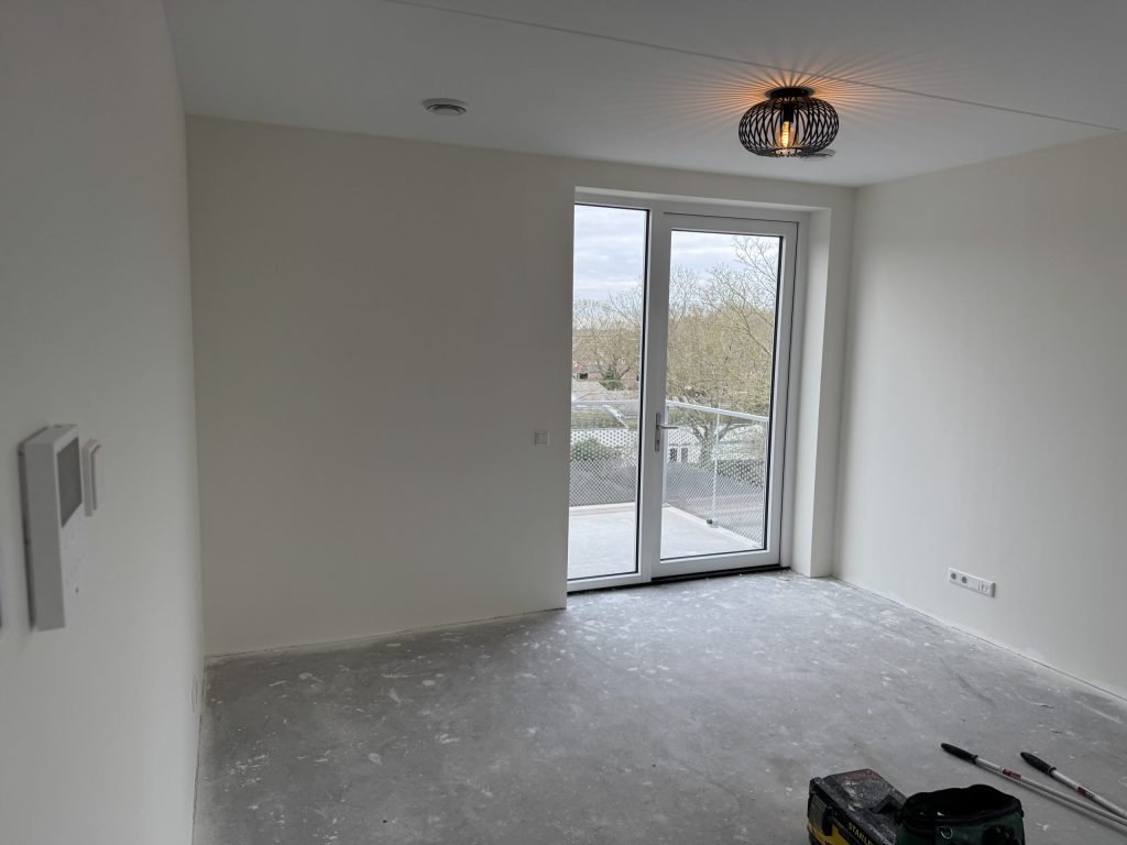 Lege kamer in een nieuw appartement met een balkondeur en kale lichte wanden, kort na de oplevering