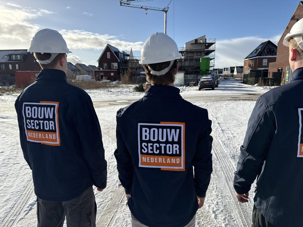 Drie vakmensen van Bouwsector Nederland met witte helm in een nieuwbouwstraat met woningen in aanbouw